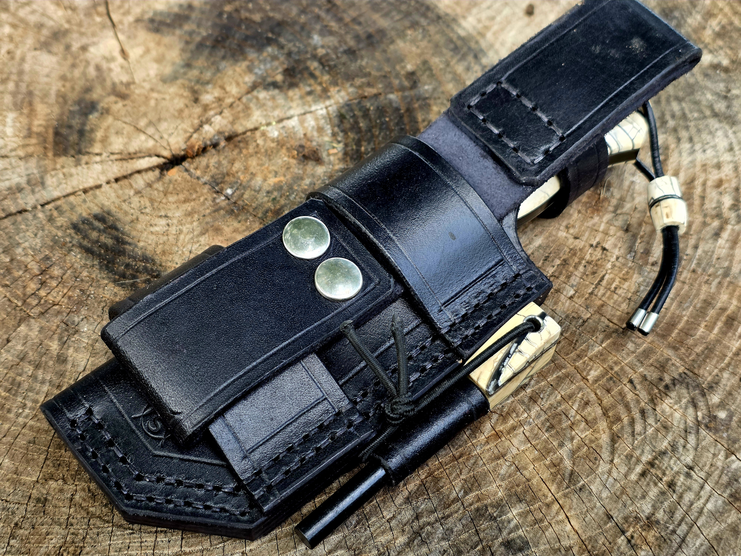 Bady K – Bushcraft-Lederscheide mit Dangler und Feuerstahl Schwarze Bushcraft-Lederscheide des Bady K mit abnehmbarem Dangler, Druckknöpfen und passendem Feuerstahl.