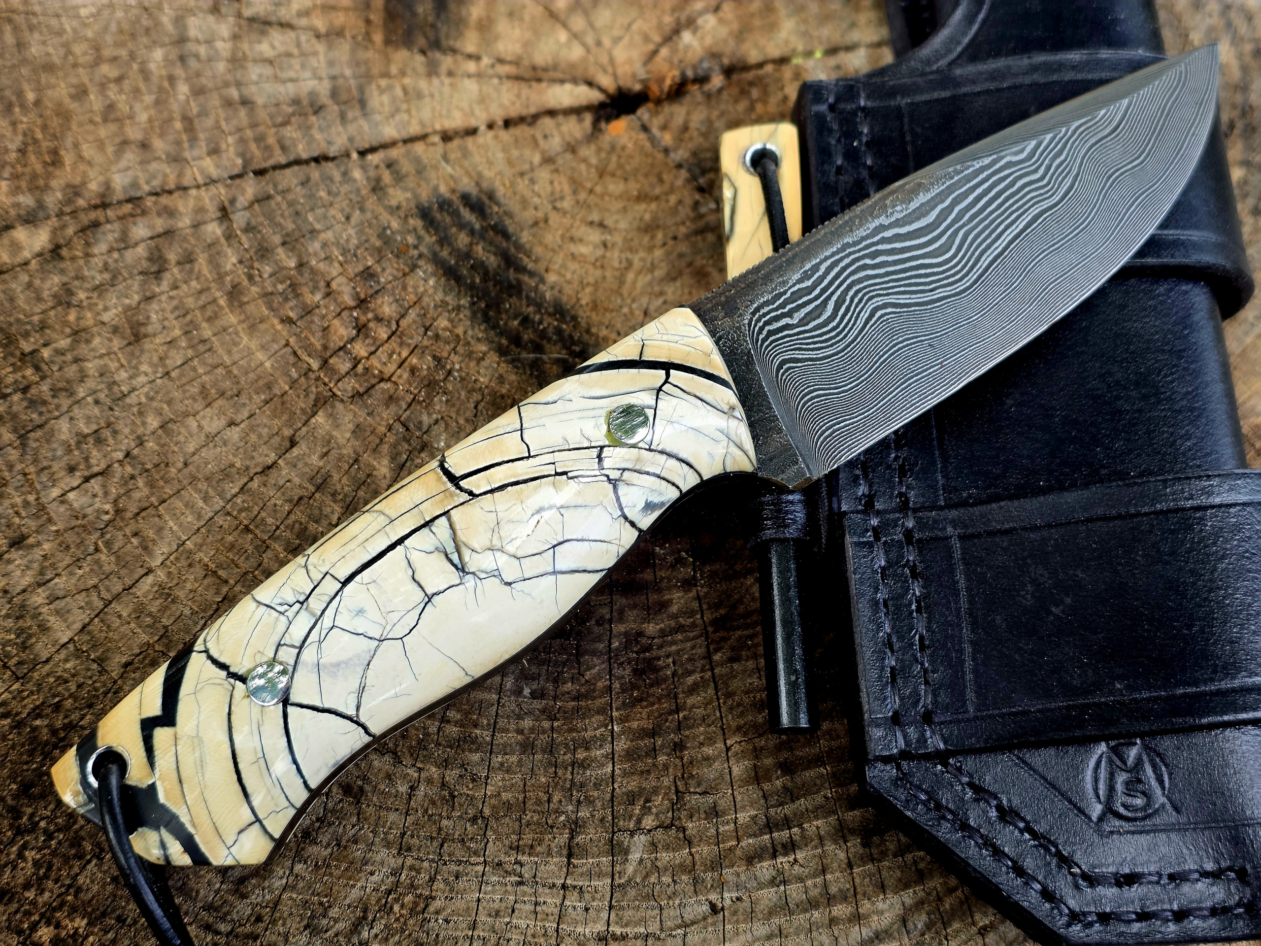 Bady K – Bushcraft Spezial mit Mammutelfenbein und Damast Handgefertigtes Bady K Bushcraftmesser mit Paschinger-Damastklinge, hellem Mammutelfenbein-Griff und schwarzer Lederscheide mit Feuerstahl.